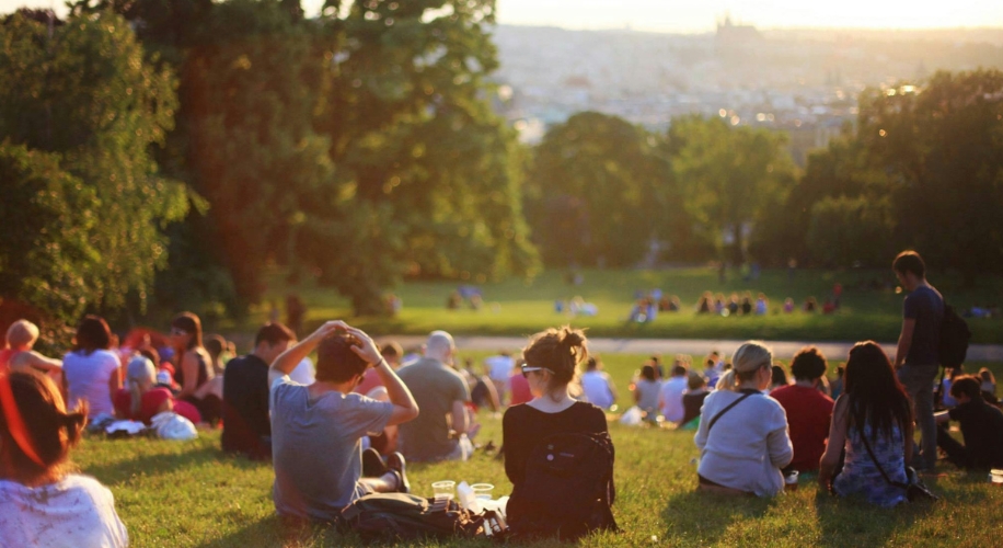 People sitting on a grassy hill in a park during sunset.