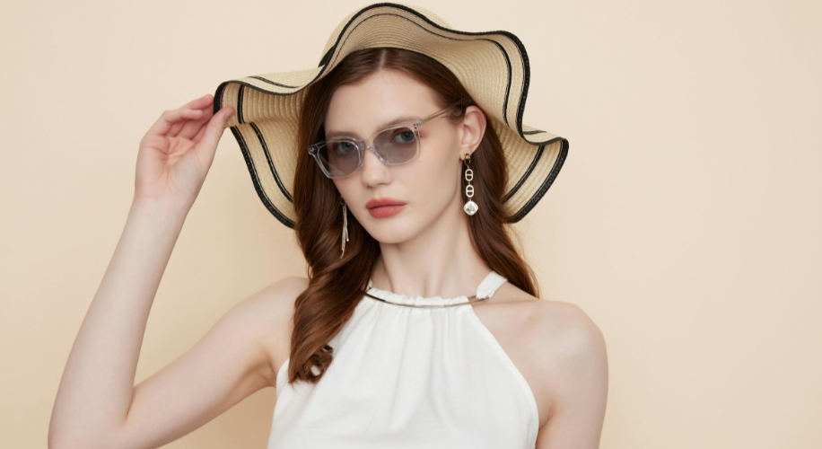 Woman wearing a wide-brimmed straw hat, clear-framed sunglasses, and drop earrings.