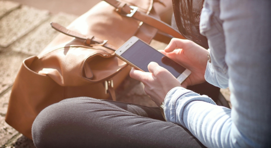 Person using a smartphone with a brown leather bag nearby.