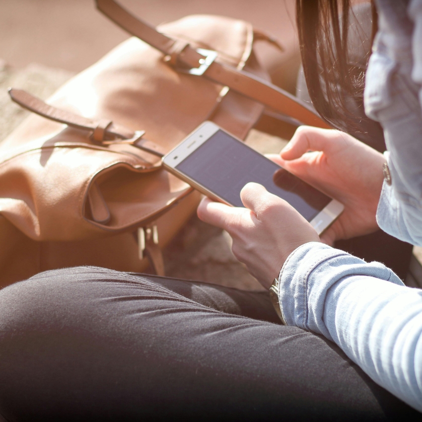 Person using a smartphone outdoors, with a tan bag nearby.