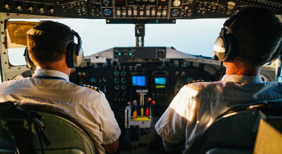 Two pilots wearing headphones in an airplane cockpit, controlling the aircraft.