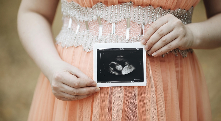 A person holding an ultrasound photo against a peach-colored, beaded dress.