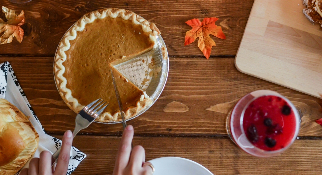 Sliced pumpkin pie with a fork and knife on a wooden table.