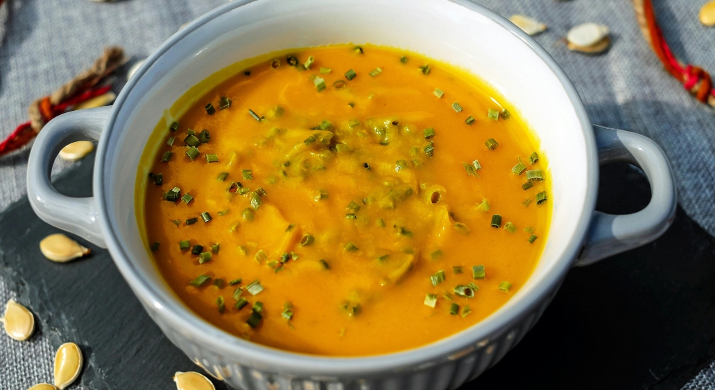 Pumpkin soup garnished with chopped chives in a gray bowl.