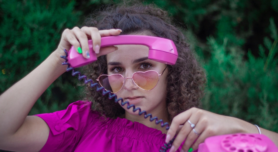 Pink rotary phone, woman holding the receiver, wearing heart-shaped sunglasses.