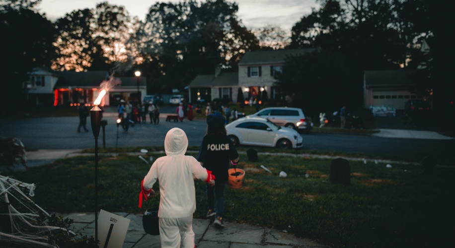 Children trick-or-treating, one in a white costume, another in a police jacket, carrying candy buckets.