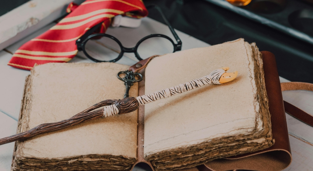 Rustic notebook with a magical-style wand pen on top, accompanied by round glasses.