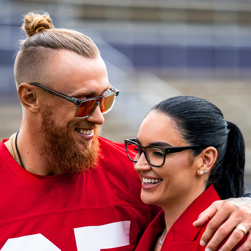 Two people wearing stylish glasses, smiling in bright natural light.