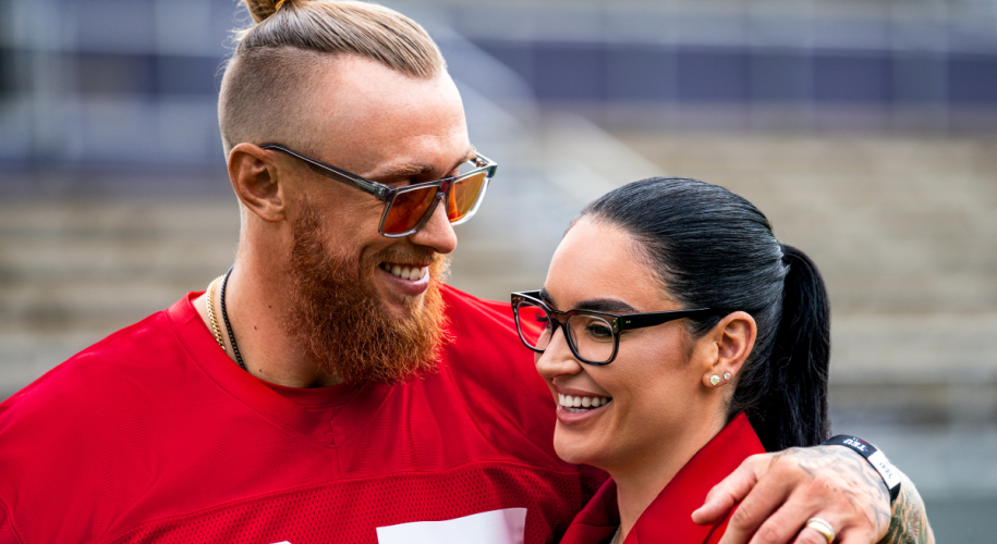 Two people wearing stylish glasses, one with red sports jersey and another in a red blazer, smiling.