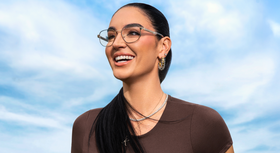 Woman wearing glasses, hoop earrings, and layered necklaces against a blue sky.