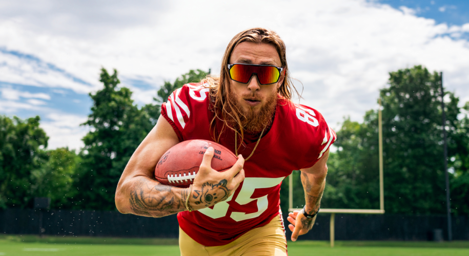 Football player wearing a red jersey with number 85 and sunglasses, holding a football. 