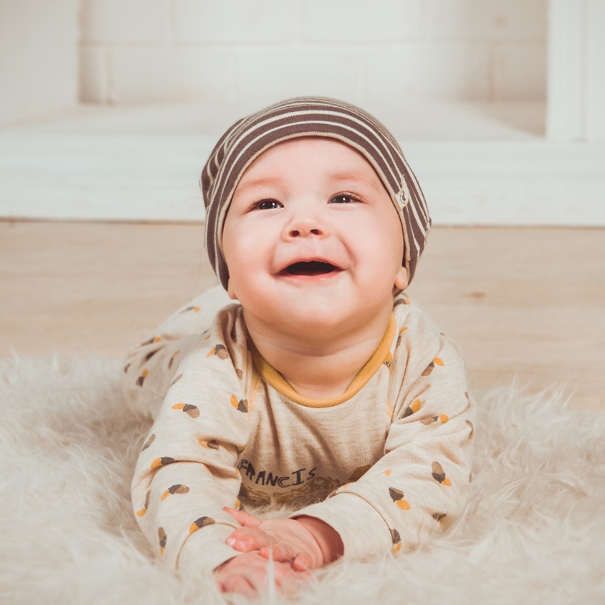 Smiling baby wearing a striped hat and patterned onesie.