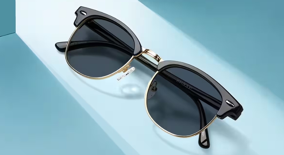 Black and gold sunglasses with dark lenses on a light blue surface.