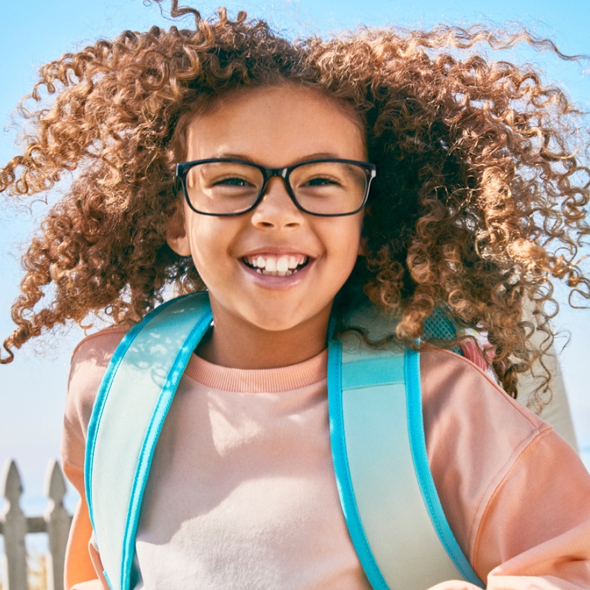 Child smiling wearing glasses and a blue backpack.