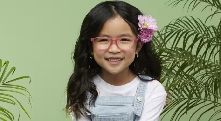 Girl wearing pink glasses with a pink flower in her hair, smiling.