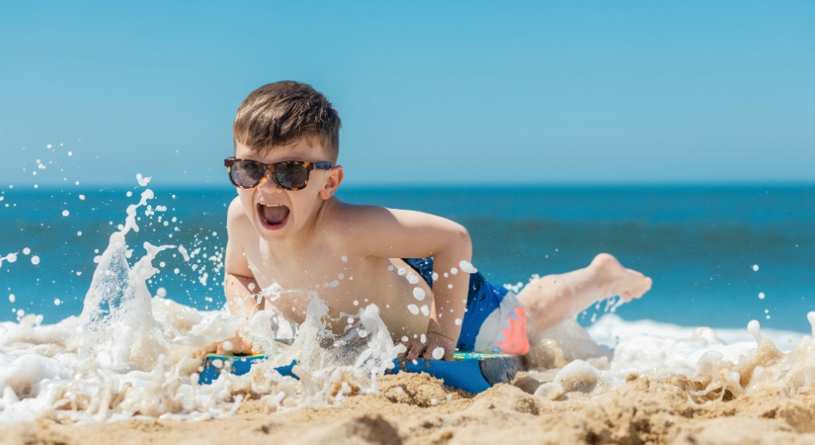 Child wearing sunglasses, enjoying the beach waves on a boogie board.