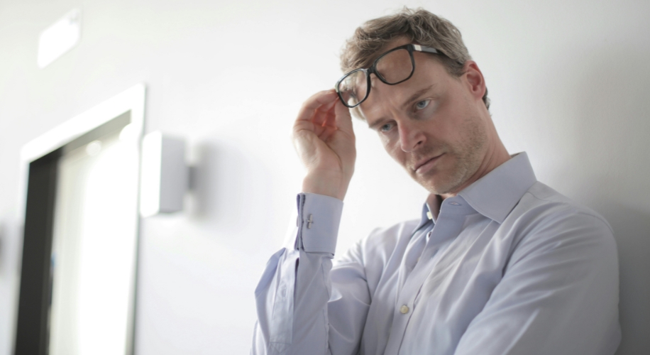 Man adjusting eyeglasses while looking at the camera, wearing a light blue shirt.