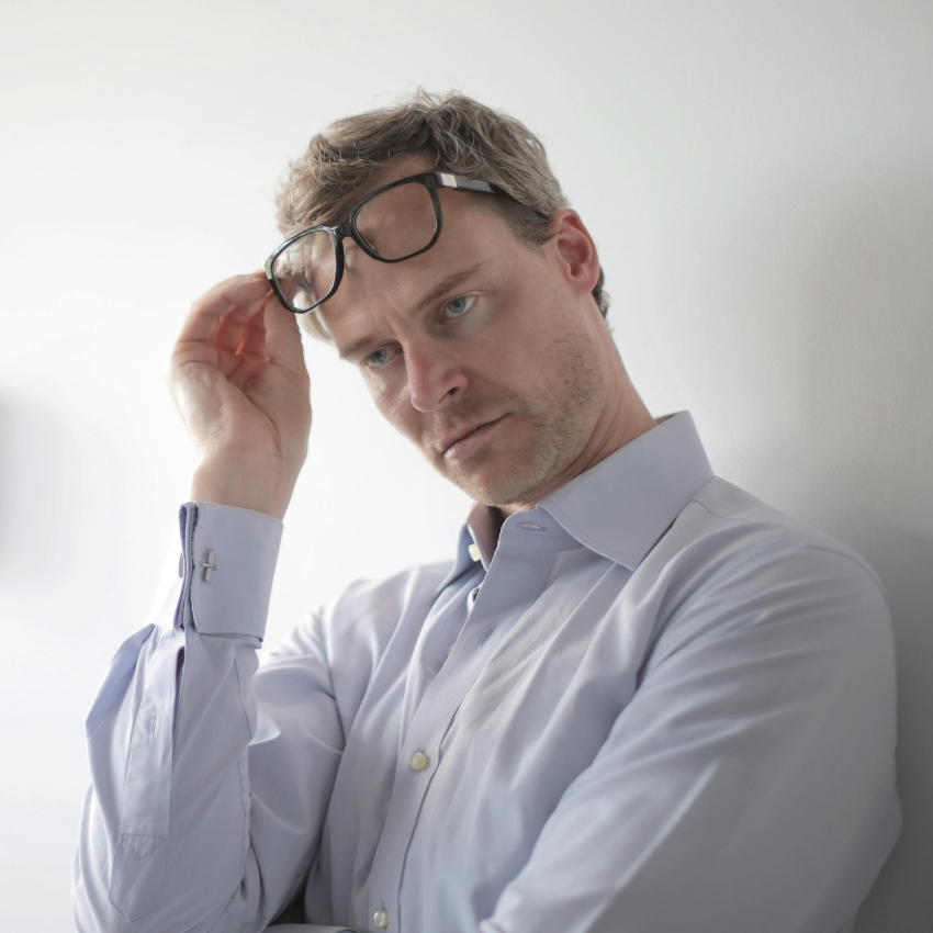 Man adjusting black-framed eyeglasses while wearing a light blue collared shirt.